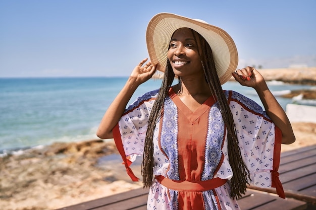 Junge afroamerikanische Frau mit Sommerhut steht am Strand