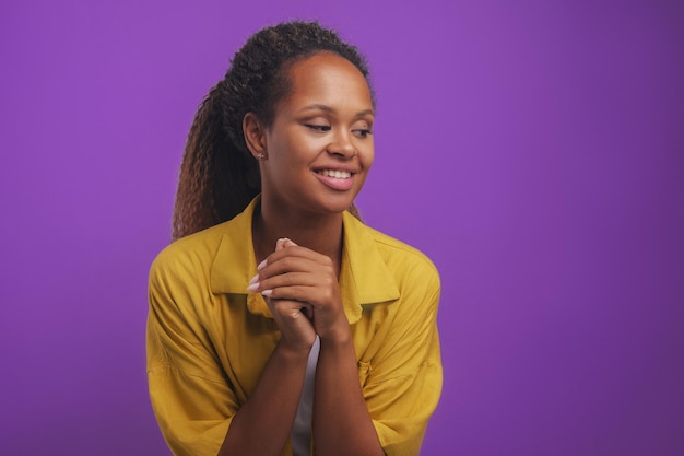 Junge afroamerikanische Frau mit süßem Lächeln, die die Hände vor der Brust umklammert