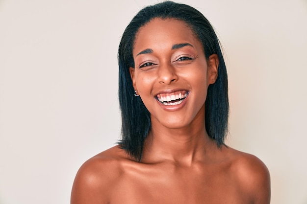 Junge afroamerikanische Frau steht oben ohne, zeigt Haut, lächelt und lacht laut, weil sie einen lustigen, verrückten Witz macht