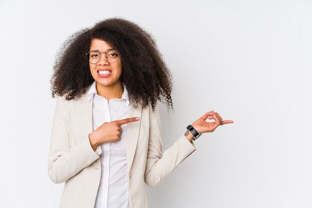 Junge afroamerikanische Geschäftsfrau schockiert, die mit Zeigefingern auf einen Kopienraum zeigt.