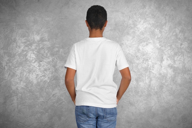 Junge afroamerikanische Junge in weißem T-Shirt steht gegen eine texturierte Wand