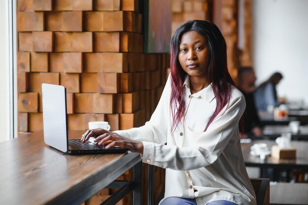 Junge afroamerikanische Mädchen sitzen im Restaurant und tippen auf ihrem Laptop Hübsches Mädchen, das am Computer im Café arbeitet