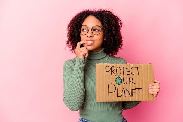 Junge afroamerikanische Mischrassenfrau, die einen Schutz unseres Planetenkartons hält, entspannte das Denken über etwas, das einen Kopienraum betrachtet.