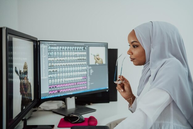 Junge afroamerikanische moderne muslimische Geschäftsfrau mit Schal an einem kreativen, hellen Büroarbeitsplatz mit großem Bildschirm. Hochwertiges Foto