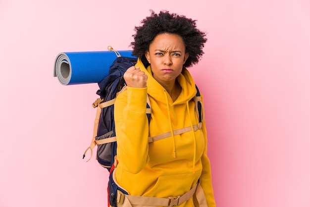 Junge afroamerikanische Rucksacktouristenfrau isoliert, die Faust, aggressiven Gesichtsausdruck zeigend zeigt.