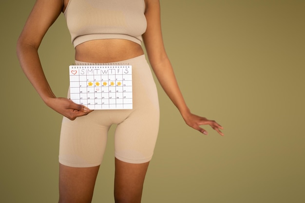 Junge afroamerikanische schlanke Dame in Sportbekleidung zeigt Kalender auf beigem Studiohintergrund zugeschnitten