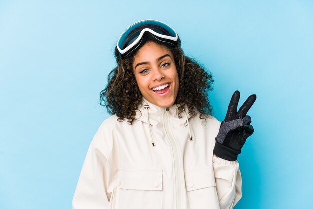 Junge afroamerikanische Skifahrerin isoliert freudig und sorglos, ein Friedenssymbol mit den Fingern zeigend.