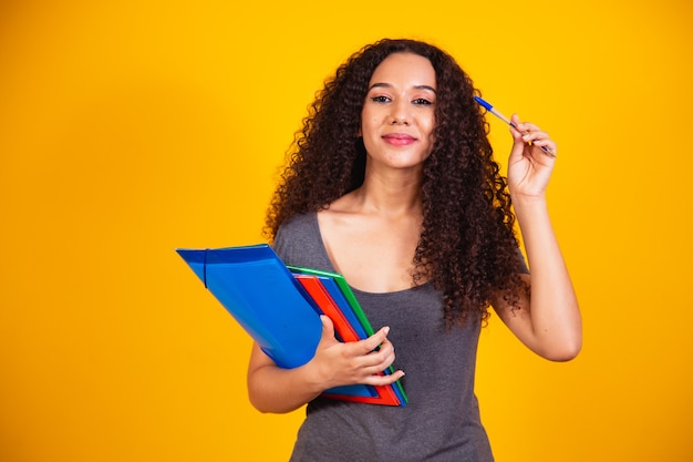 Junge afroamerikanische Teenager-Studentin in Freizeitkleidung, die Bücher auf gelbem Hintergrund Studioportrait isoliert hält. Bildung an der High School University College-Konzept. Kopienraum nachmachen