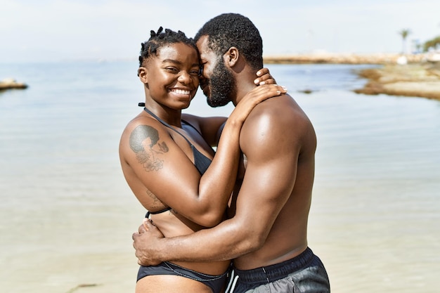 Junge afroamerikanische Touristenpaare in Badebekleidung umarmen sich am Strand.