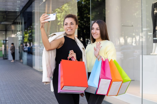 Junge afroamerikanische und kaukasische Frauen mit bunten Taschen, die Selfies am Telefon machen