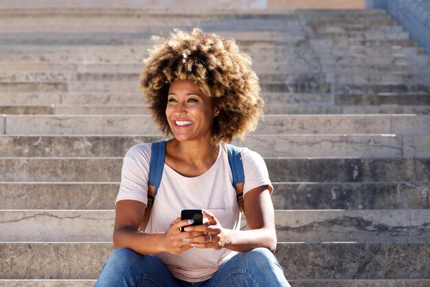 Junge afroe-amerikanisch Frau, die auf Treppe mit Handy sitzt und weg schaut