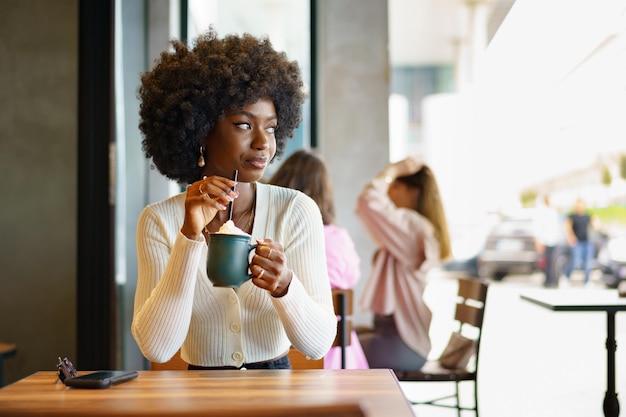 Junge afrofrau, die pause macht und kaffee im café trinkt