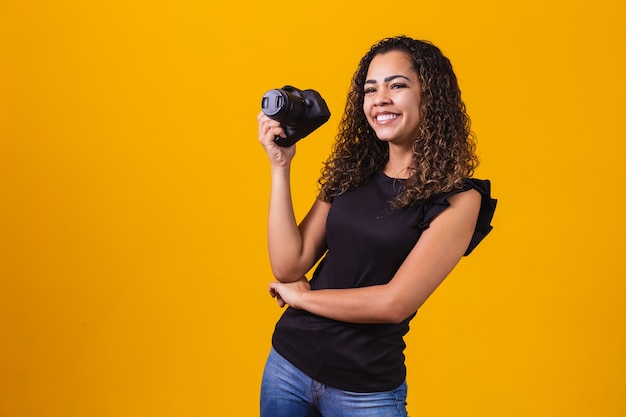 Junge Afrofrauenphotographie auf gelbem Hintergrund, der eine Fotokamera hält.