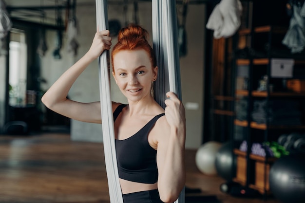 Junge aktive Frau im Trainingsanzug, die auf einer Fly-Yoga-Hängematte sitzt