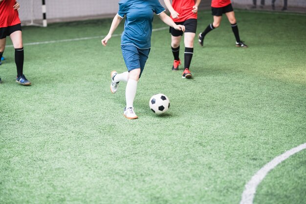 Junge aktive Frauen in der roten und blauen Sportuniform, die Ball während des Fußballspiels auf dem Feld angreift