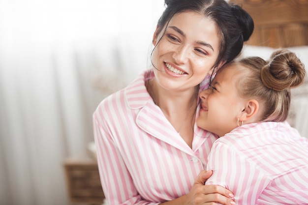 Junge aktive Mutter und ihre kleine Tochter haben Spaß zusammen zu Hause im Schlafzimmer im Schlafanzug