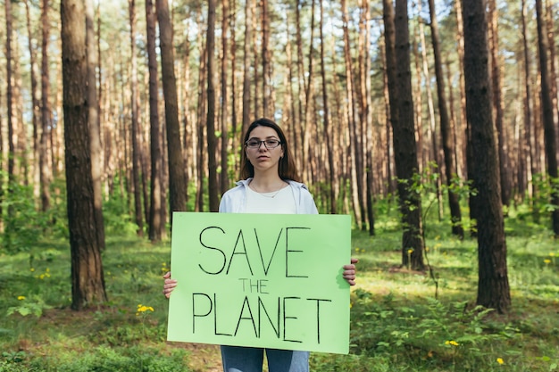 Junge Aktivistin, die mit einem Plakat im Wald steht, um den Planeten zu retten, eine Freiwillige kämpft mit Abholzung