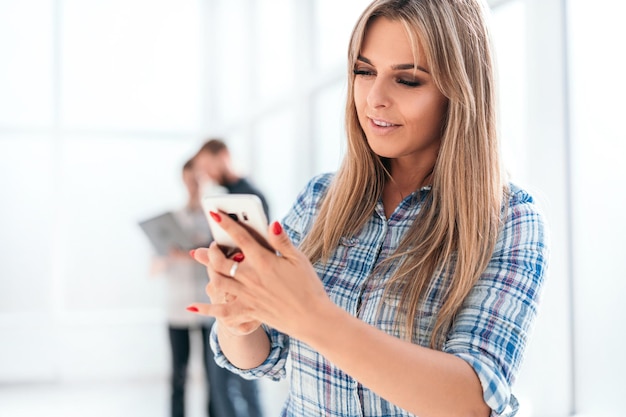 Junge Angestellte benutzt ein Smartphone, das im Büro steht. Foto mit Textfreiraum