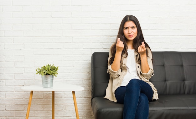 Junge arabische Frau, die auf dem Sofa zeigt sitzt, dass sie kein Geld hat.