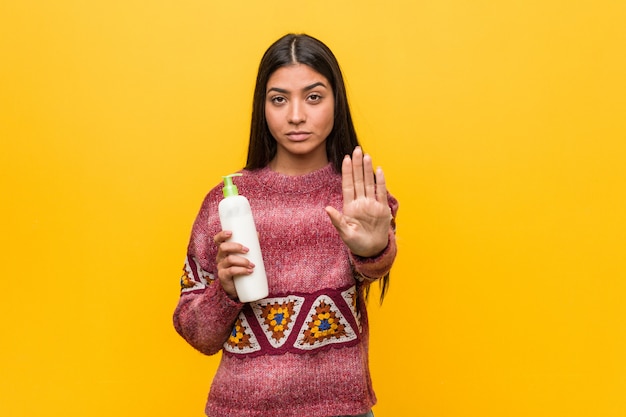 Junge arabische Frau, die eine Sahneflasche steht mit der ausgestreckten Hand zeigt das Stoppschild und verhindert Sie hält.