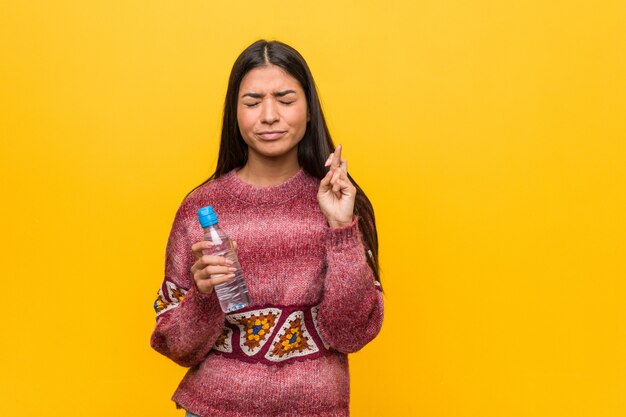 Junge arabische Frau, die Finger einer Wasserflaschenüberfahrt für das Haben des Glücks hält