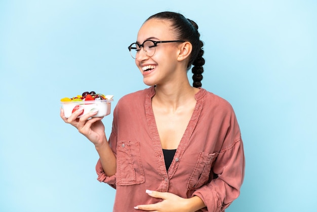 Junge arabische Frau mit einer Obstschale isoliert auf blauem Hintergrund, die viel lächelt
