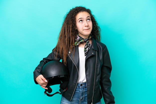 Foto junge arabische frau mit motorradhelm isoliert auf blauem hintergrund und nach oben schauend