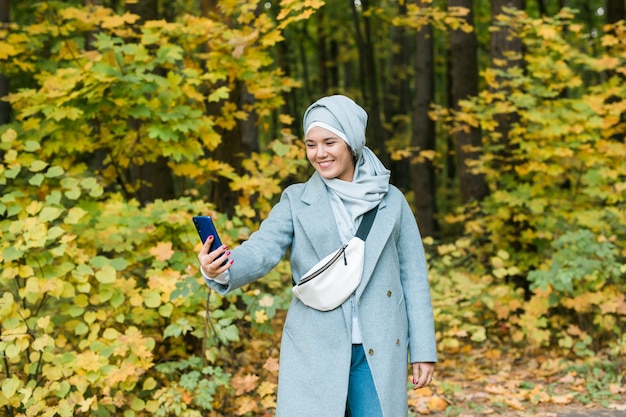 Junge arabische muslimische Frau in Hijab-Kleidung beim Selfie-Schuss auf dem Handy im Park. Menschen religiöses Lifestyle-Konzept. Platz kopieren.