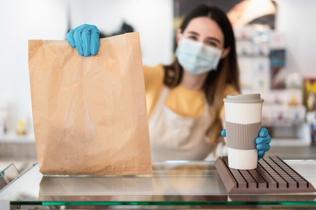 Junge Arbeiterfrau, die Essen zum Mitnehmen mit Gesichtsmaske liefert