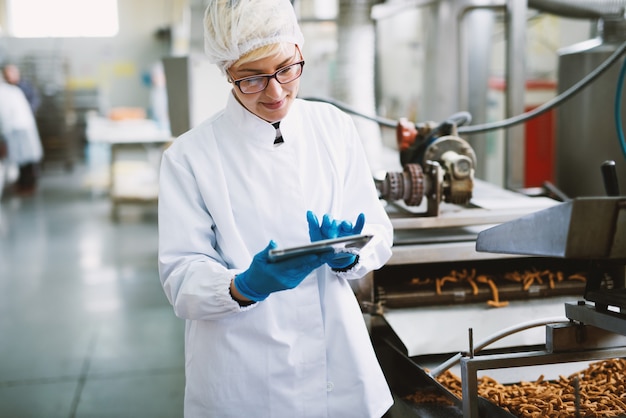 Junge Arbeiterin in steriler Kleidung überprüft die Qualität der Produkte in der Lebensmittelfabrik.