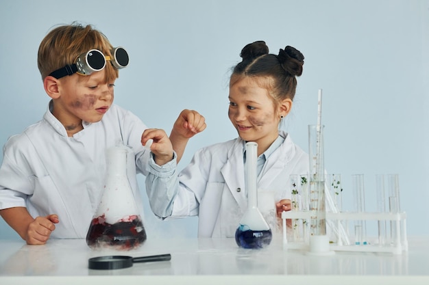 Foto junge arbeitet mit flüssigkeit in reagenzgläsern. kinder in weißen kitteln spielen wissenschaftler im labor, indem sie geräte verwenden