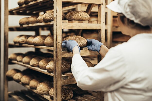 Junge Arbeitnehmerin, die in der Bäckerei arbeitet. Sie stellt Brot ins Regal.
