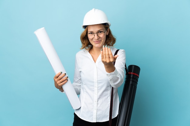 Junge Architektin georgische Frau mit Helm und Blaupausen über isoliertem Hintergrund, die einladen, mit der Hand zu kommen. Schön, dass du gekommen bist