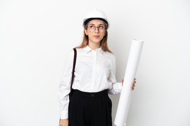 Junge Architektin mit Helm und Halteplänen lokalisiert auf weißer Wand und nach oben schauend