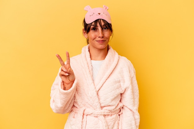 Foto junge argentinische frau, die einen pyjama trägt, der auf gelbem hintergrund isoliert ist und die nummer zwei mit den fingern zeigt.