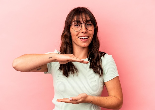 Junge argentinische Frau isoliert auf rosa Hintergrund, die etwas mit beiden Händen hält, Produktpräsentation.