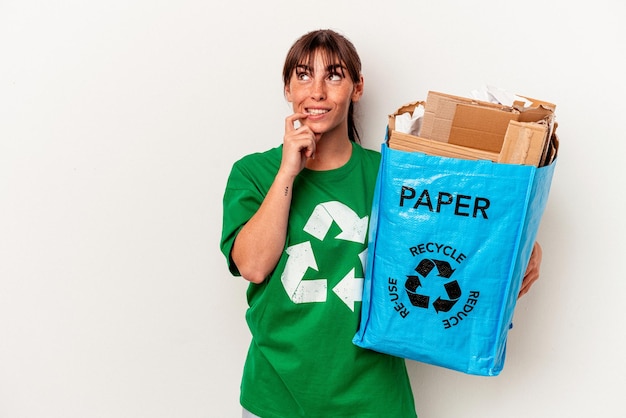 Junge argentinische Frau recyceltes Papier isoliert auf gelbem Hintergrund entspanntes Denken an etwas, das einen Kopierraum betrachtet.