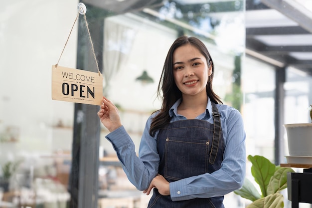 Junge Asia Managerin, die ein Schild von geschlossen auf offen am Türcafé ändert und nach draußen auf Kunden wartet, nachdem sie gesperrt wurde