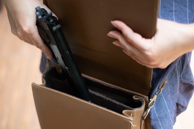 Junge Asiatin, die eine Waffe in ihre Handtasche steckt Frauenhand, die eine Pistole aus der Tasche zieht