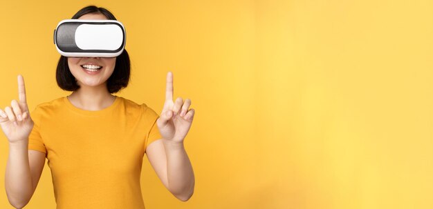 Junge asiatin, die in vr spielt, indem sie eine virtual-reality-brille verwendet, die ein gelbes t-shirt gegen studio b trägt