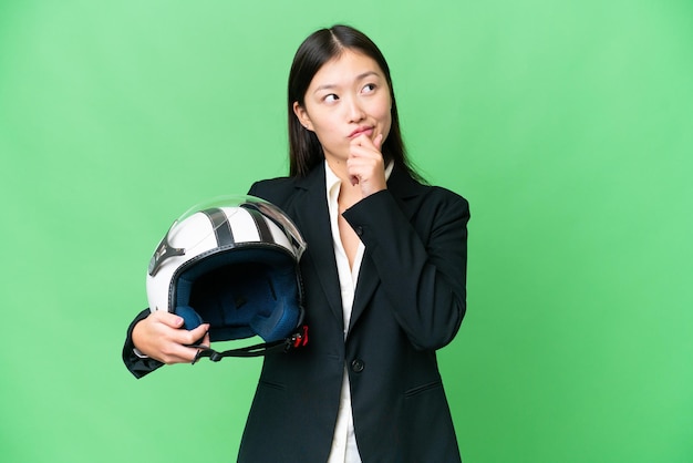 Junge Asiatin mit Motorradhelm vor isoliertem Chroma-Key-Hintergrund und Blick nach oben