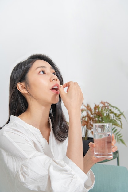 Junge Asiatin nimmt Medizin im Wohnzimmer ein