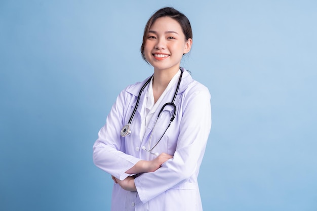 Junge asiatische Ärztin, die auf blauem Hintergrund steht