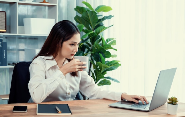 Junge asiatische begeisterte Geschäftsfrau am modernen Schreibtisch mit Laptop