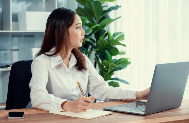 Junge asiatische begeisterte Geschäftsfrau am modernen Schreibtisch mit Laptop