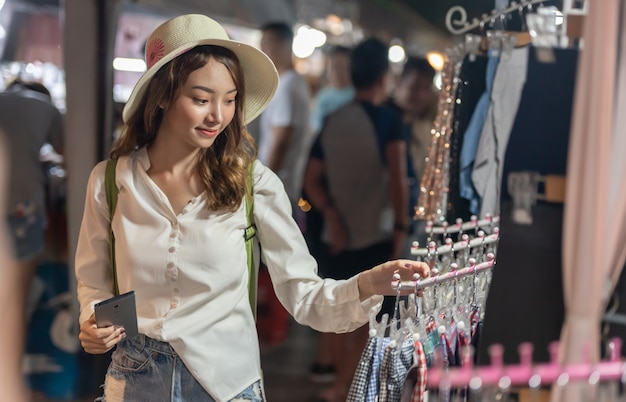 Junge asiatische Einkaufsfrau, die Stoffe am Nachtmarkt wählt und kauft