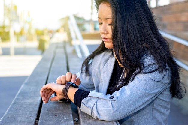 Junge asiatische erfolgreiche Geschäftsfrau im Anzug, die mit Smartwatch in der Großstadt steht