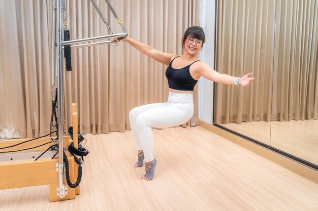 Foto junge asiatische frau arbeitet während ihres fitness-dexercise-trainings an einer pilates-reformer-maschine