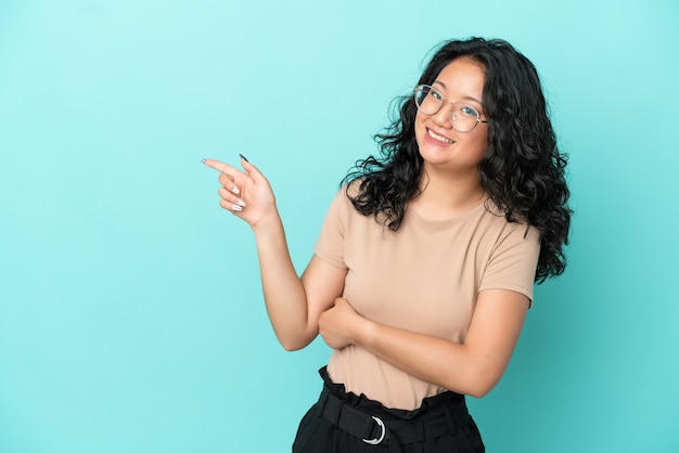 Junge asiatische Frau auf blauem Hintergrund isoliert, die mit dem Finger zur Seite zeigt