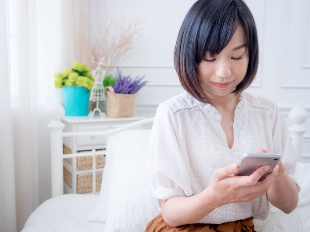 Junge asiatische Frau auf dem Bett mit Telefon